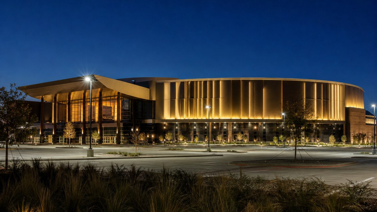 Sports venue exterior facade lit with gold architectural LED lighting and illuminated parking plaza at dusk in Texas