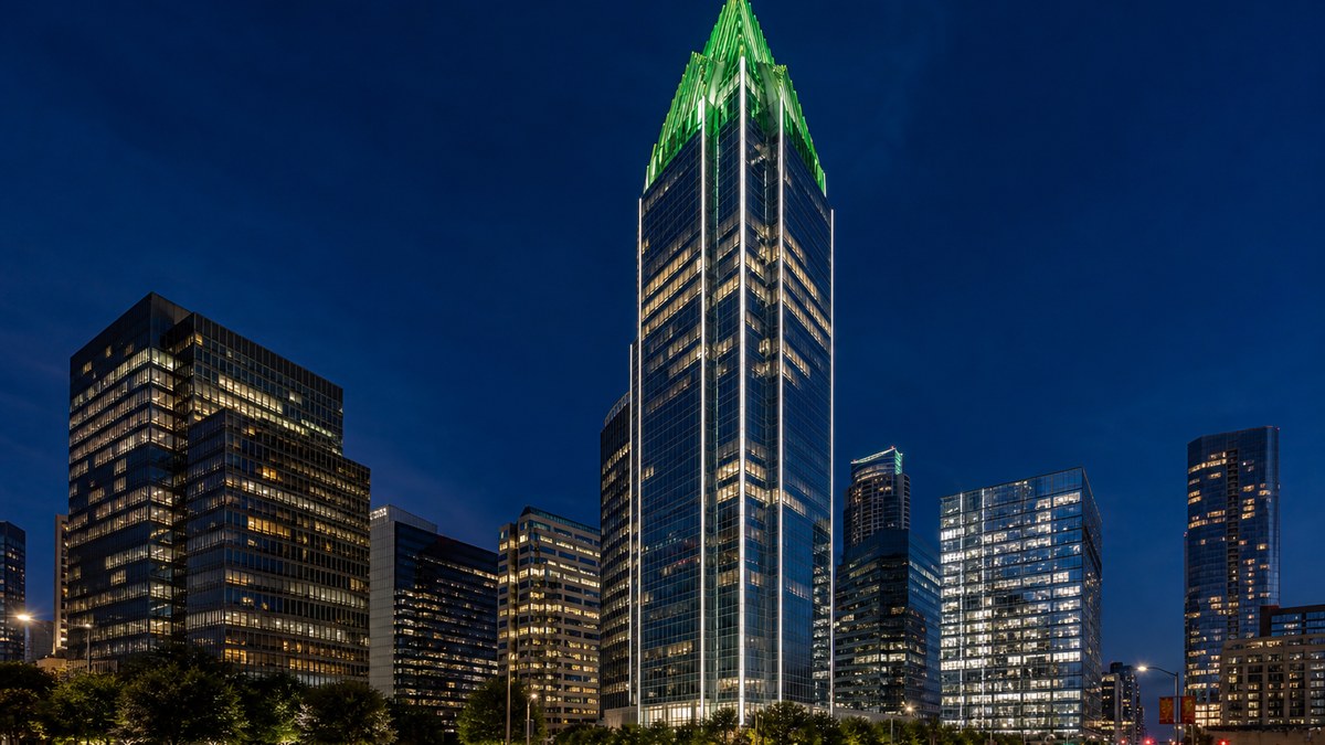 High-rise facade lighting in Dallas: glass office tower with linear LED grazing and an emerald-lit crown at blue hour