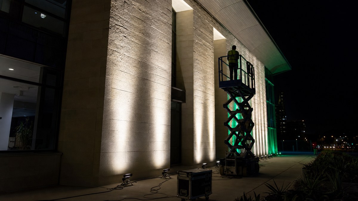 Night-time on-site lighting mockup on a Dallas building facade with test LED grazers being aimed from a lift