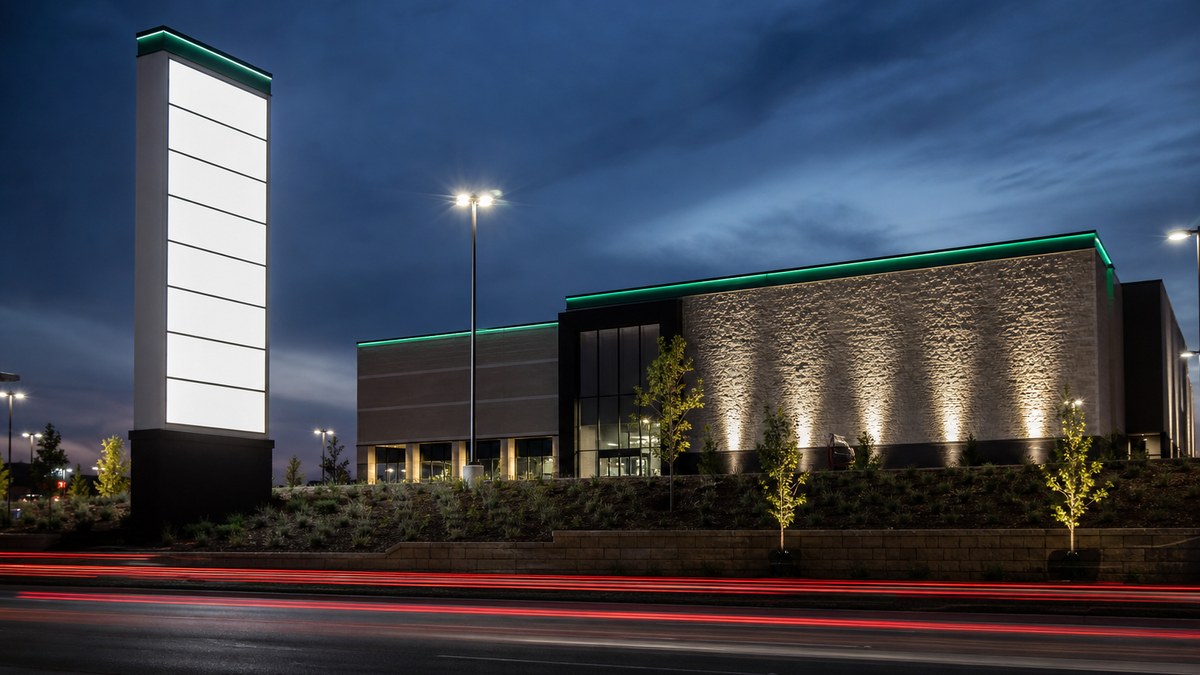 Retail center anchor building and LED pylon sign at blue hour with green-accented architectural facade lighting along a Texas highway frontage road