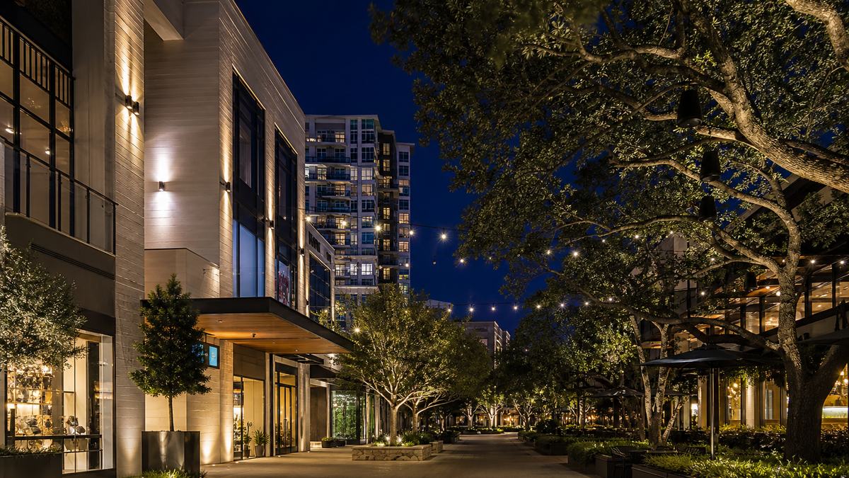 Shopping center LED lighting in Dallas: open-air lifestyle center promenade at dusk with architectural facade lighting, string lights and illuminated storefronts