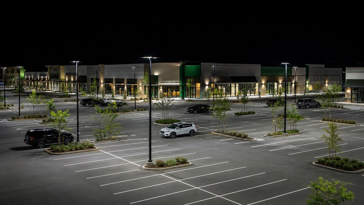 Shopping center parking lot at night with full-cutoff LED area lights providing uniform, low-glare illumination in front of illuminated retail storefronts